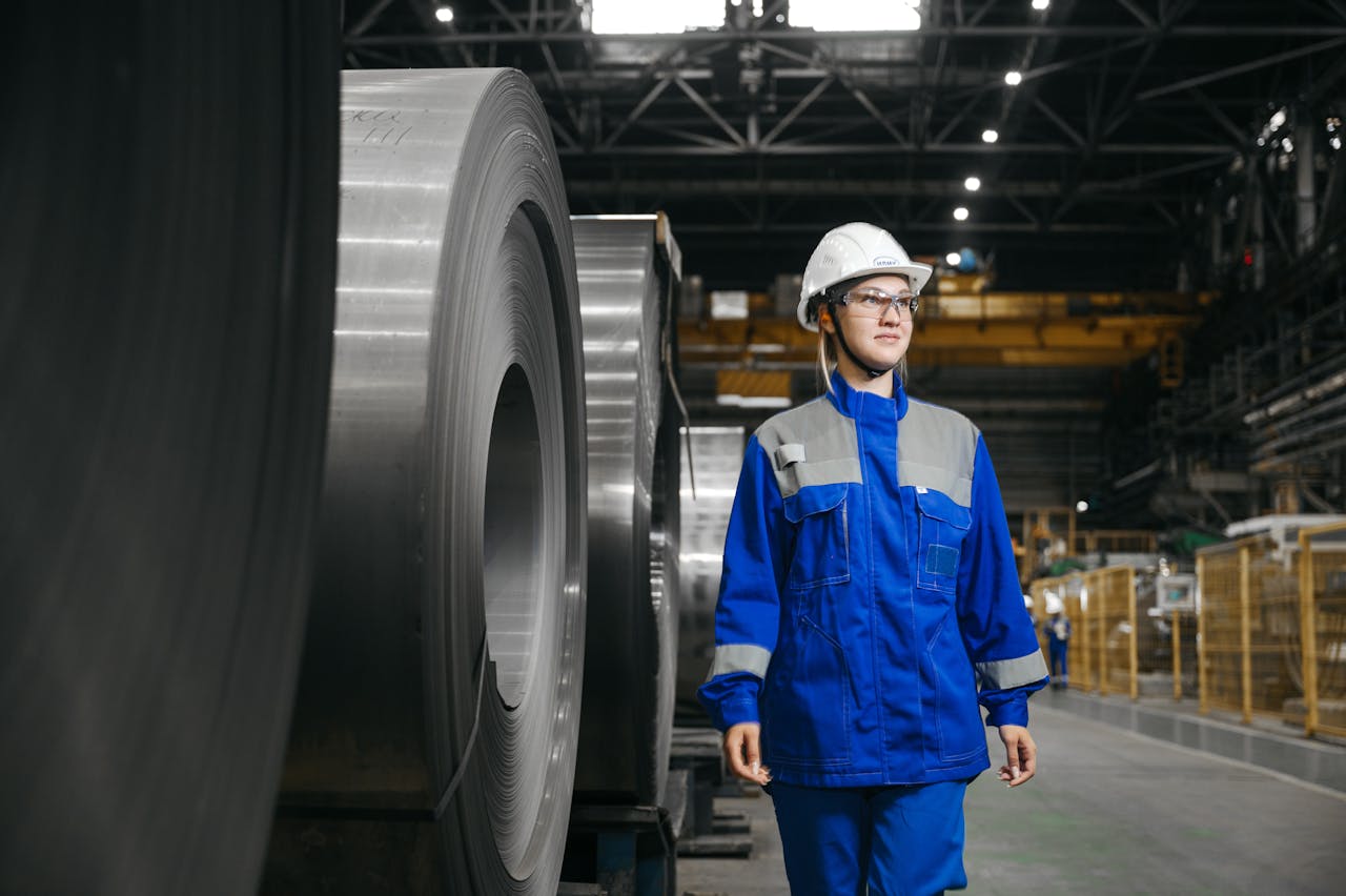 Female industrial worker in protective gear at a steel manufacturing facility.